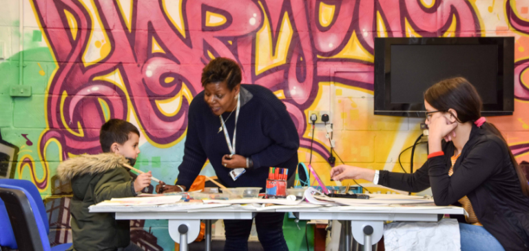Tutor supporting children with an art activity in front of a colourful graffiti art mural