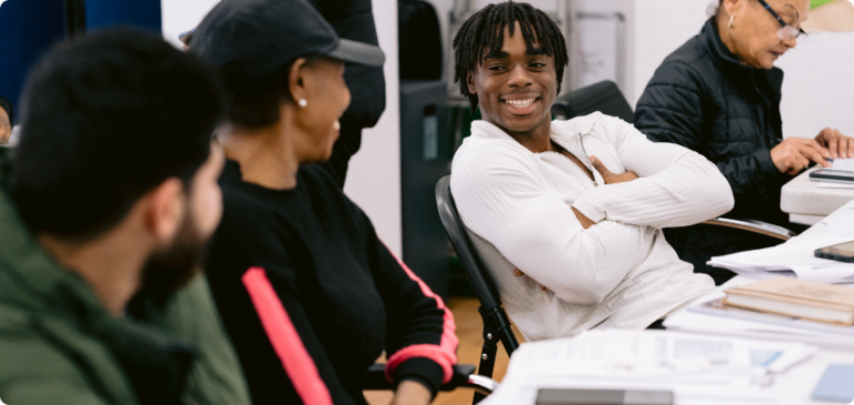 Young man folding his arms smiling and talking with others in a classroom