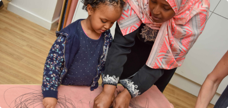 Woman helping a young child draw on large pink paper
